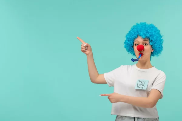 chica-payaso-dia-inocentes-silbar-ambas-manos-apuntando-izquierda-gafas-sol-azules-traje-divertido-cabello-azul-min_11zon